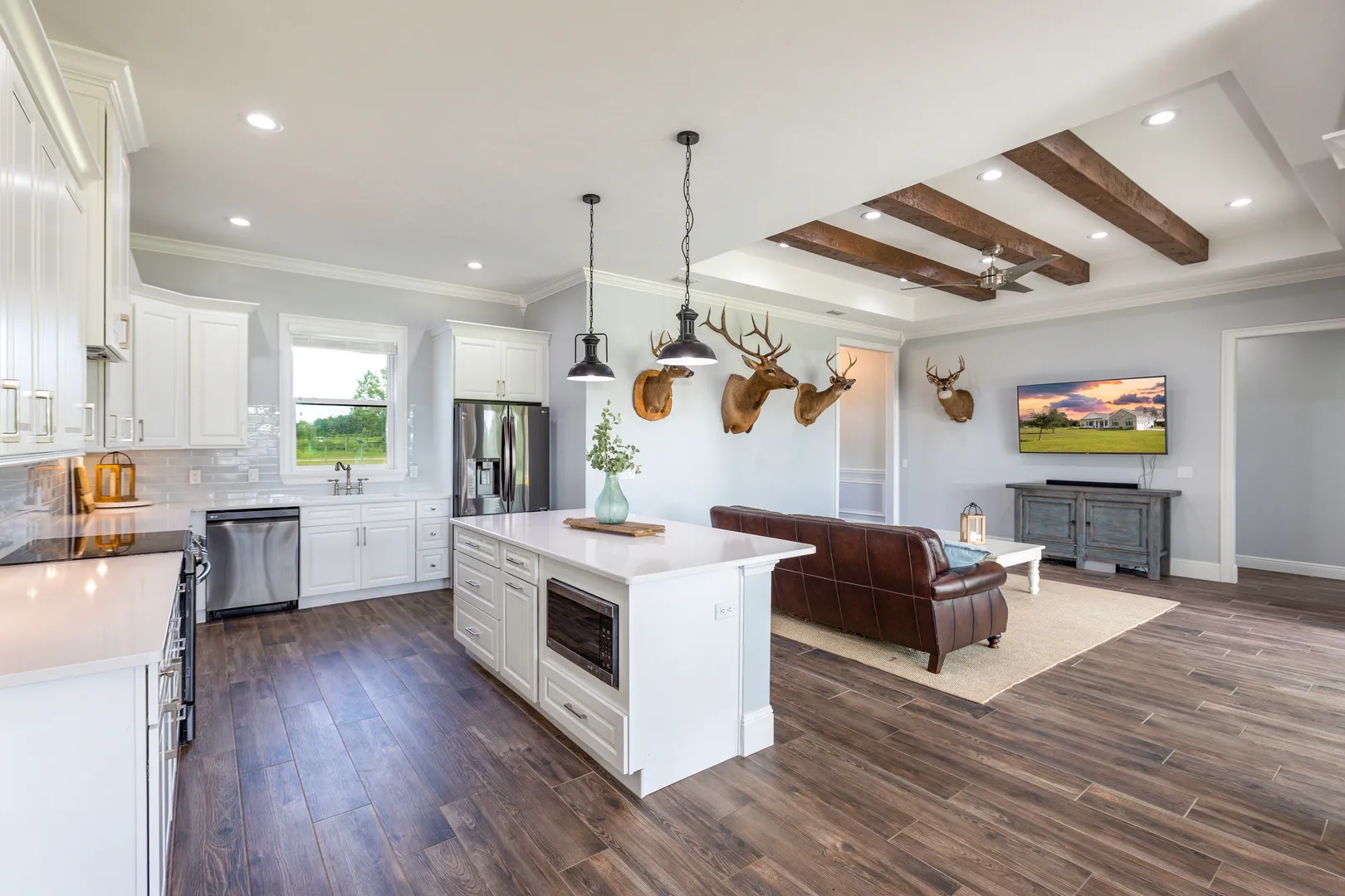 An open kitchen with white cabinets and a large island, looking into the living room.